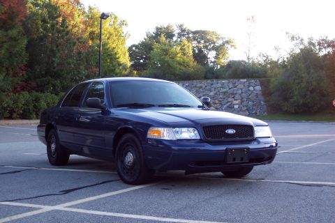 2001 Ford Crown Victoria - A dark blue Ford Crown Victoria is parked in an empty lot with trees in the background.