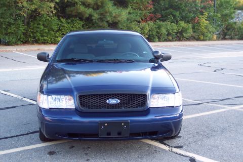 2001 Ford Crown Victoria - Front view of a dark blue 2001 Ford Crown Victoria parked in an empty lot with trees in the background.