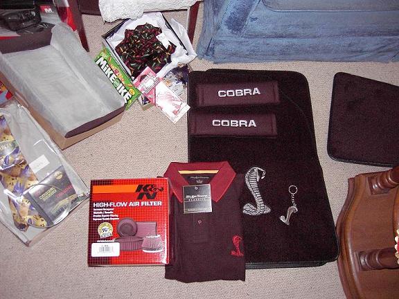 Cobra floor mats, seat belt pads, K&N air filter box, polo shirt and keychain displayed on carpet
