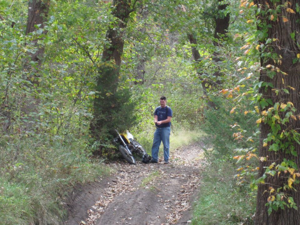 Yellow and black dirt motorcycle lying on its side on a dirt path in a wooded area