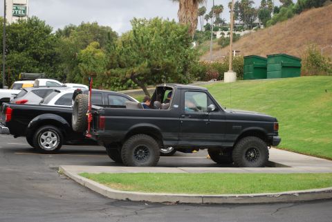 1996 Ford Bronco - Side view of a black 1996 Ford Bronco with a spare tire mounted on the back, parked in a lot.
