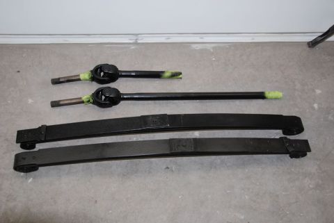 1996 Ford Bronco - Two driveshafts and two leaf springs, likely for a vehicle, are laid out on a concrete surface.