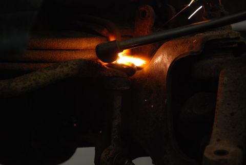 1996 Ford Bronco - A mechanic is welding a rusty suspension component on a vehicle.