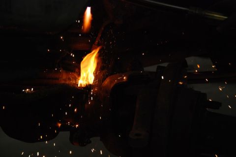 1996 Ford Bronco - A welding torch creates a bright flame and sparks while working on a dark metal component, likely a vehicle part.