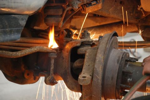1996 Ford Bronco - Mechanic uses a torch on a rusty vehicle suspension part, creating sparks.
