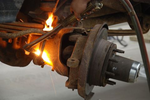1996 Ford Bronco - A cutting torch is used to heat a rusty suspension part on a vehicle, with sparks flying.