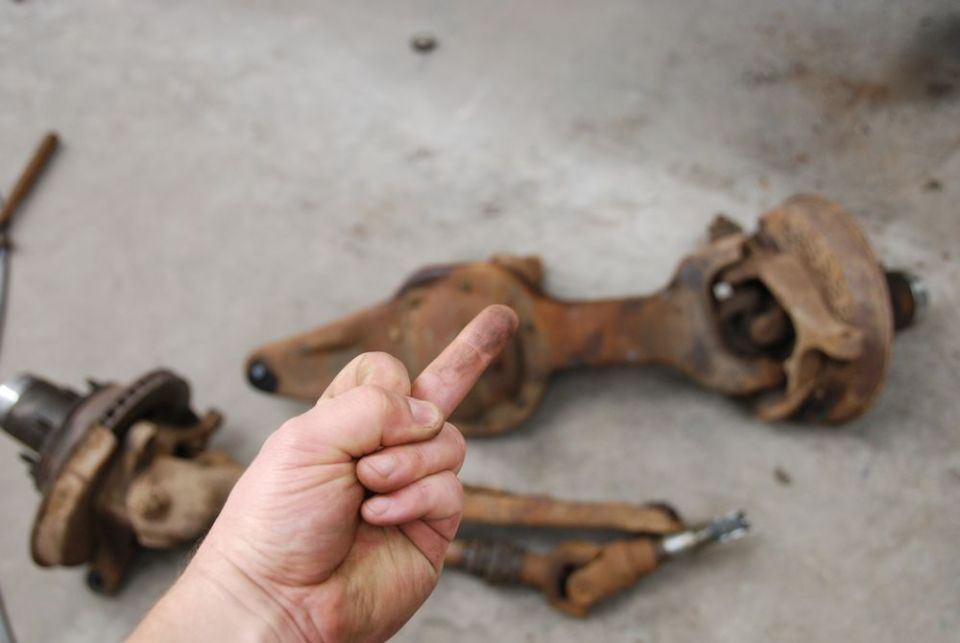 Rusty vehicle axle components on concrete floor with a hand giving the middle finger