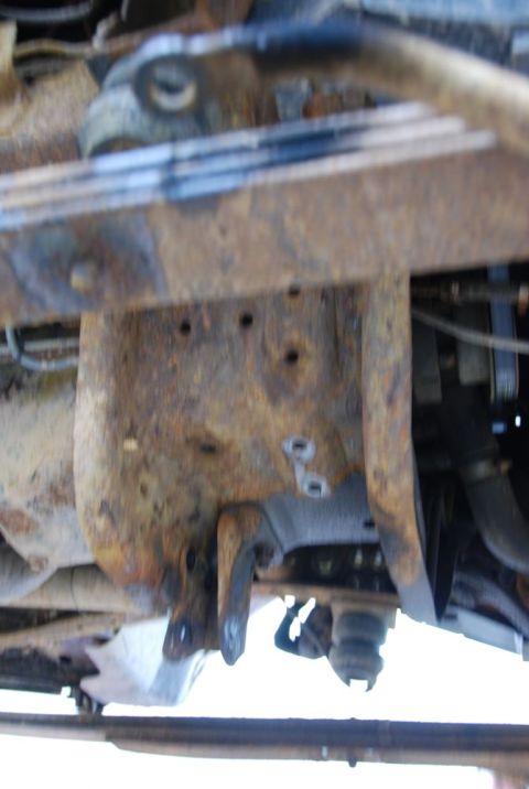 1996 Ford Bronco - Underside view of a heavily corroded vehicle frame section, showing suspension mounting points.