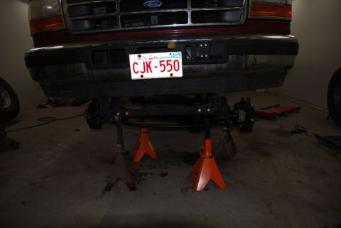 1996 Ford Bronco - Front end of a red Ford truck, possibly a F-250, is elevated on jack stands for maintenance.
