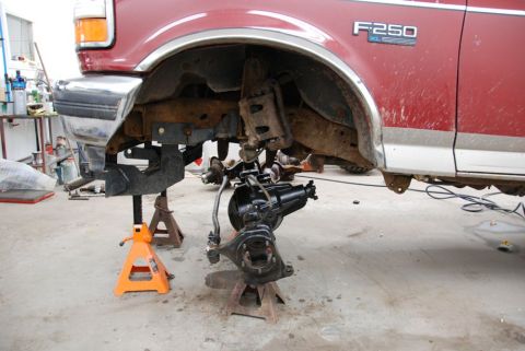 1996 Ford Bronco - A red Ford F-250 truck is shown with its front axle removed and supported by jack stands, indicating it is undergoing maintenance or repair.