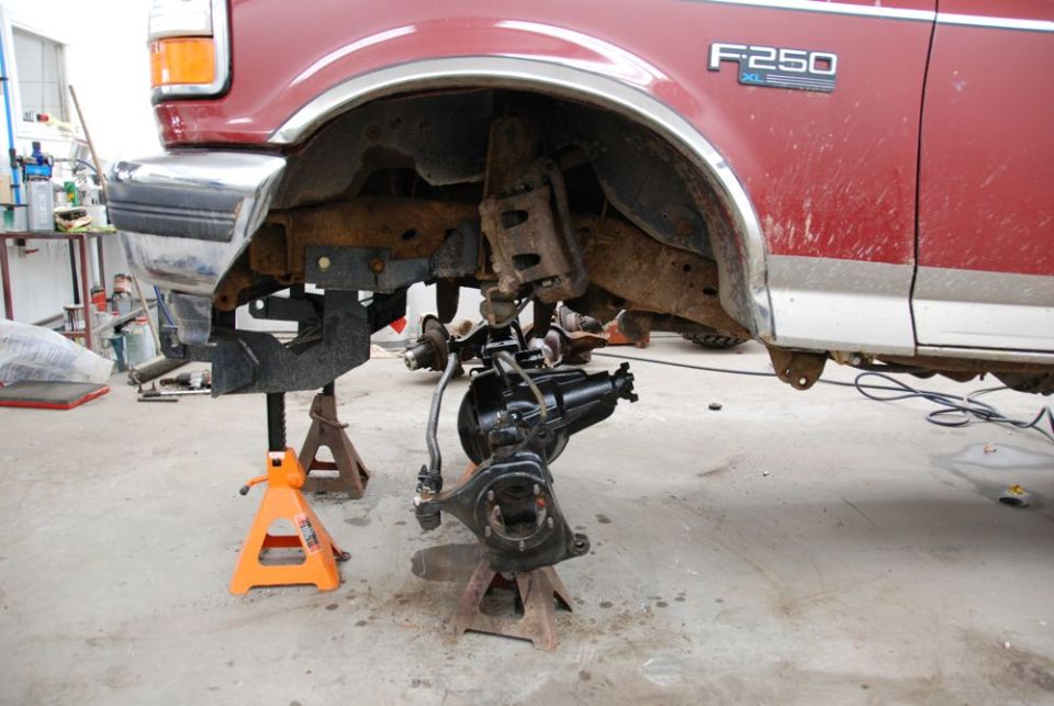 Red Ford F-250 with front axle removed, supported by jack stands