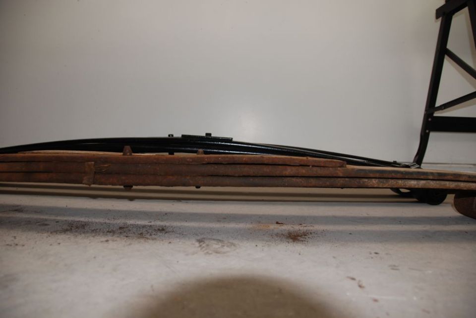 rusted leaf spring assembly with black new springs on top, leaning against a stand
