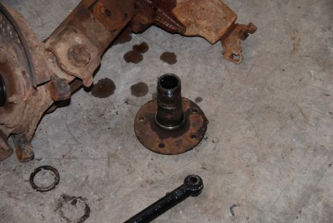 1996 Ford Bronco - Disassembled vehicle suspension components, including a hub and linkage, lie on a concrete surface.