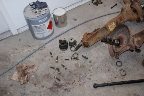 1996 Ford Bronco - Various rusty axle parts and a large drum of lubricant are laid out on a garage floor.