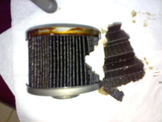 Damaged oil filter with torn filter media and oil residue