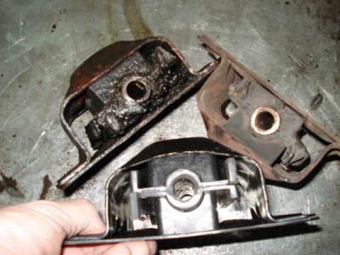 1979 Chevrolet C/K Pickup - Three engine mounts are shown, with one being held by a hand. The mounts appear worn and greasy.