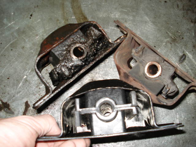 Three used engine mounts, one held by a hand, on a metal surface