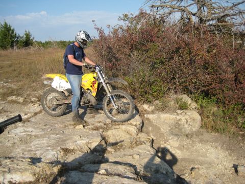 1993 Suzuki RMX250 - A rider on a yellow 1993 Suzuki RMX250 navigates a rocky trail on a sunny day.