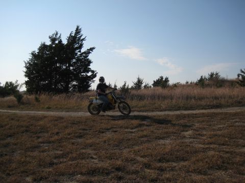 1993 Suzuki RMX250 - A person rides a dirt bike through a dry, grassy landscape under a clear blue sky.