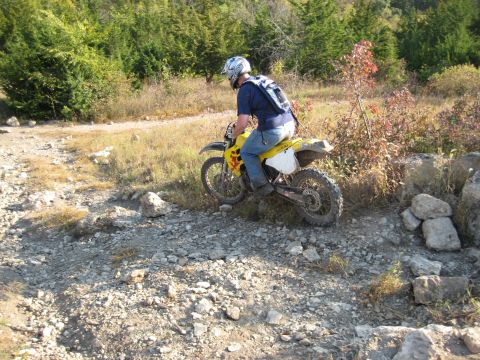 1993 Suzuki RMX250 - A person rides a dirt bike through a rough, rocky terrain on a sunny day.