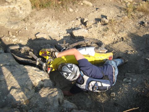 1993 Suzuki RMX250 - A rider is pinned under a yellow 1993 Suzuki RMX250 dirt bike after an apparent crash in rocky terrain.