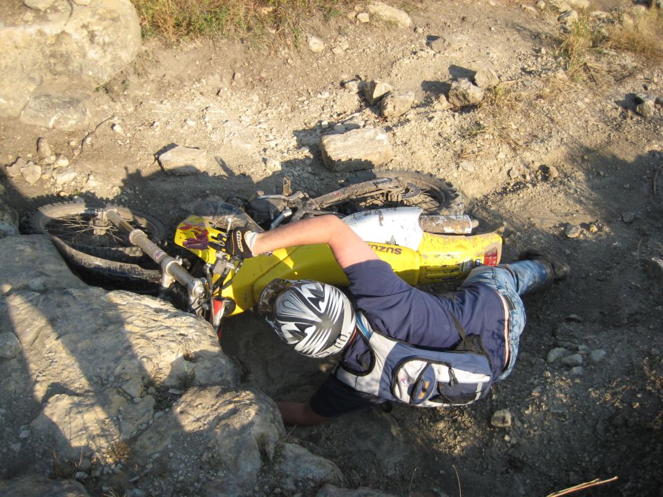 Yellow 1993 Suzuki RMX250 dirt bike on its side in rocky terrain with a rider partially underneath