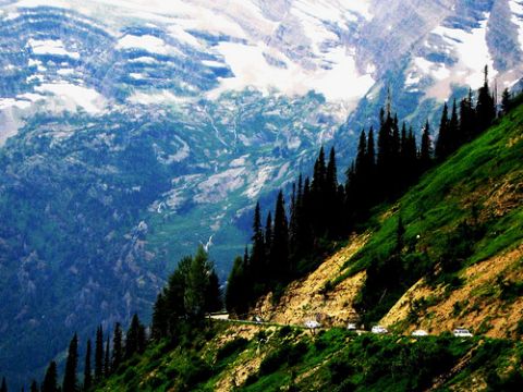 1974 Ford Ranchero - Vehicles navigate a winding road on a steep mountainside, with snow-capped peaks in the background.