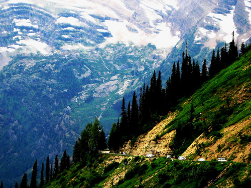 Several white vehicles drive along a mountain road