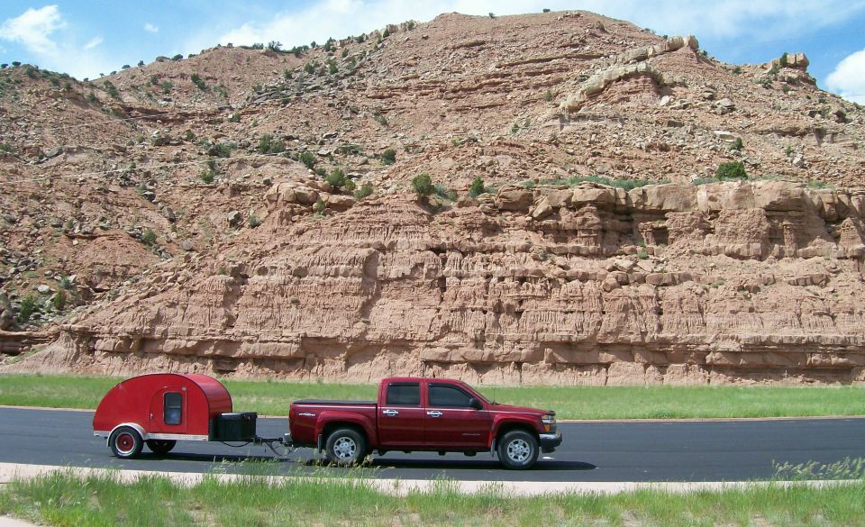 Red crew-cab pickup towing a red teardrop trailer past red rock cliffs