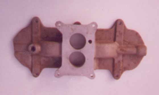 Cast iron intake manifold with two carburetor mounting holes and a central adapter plate