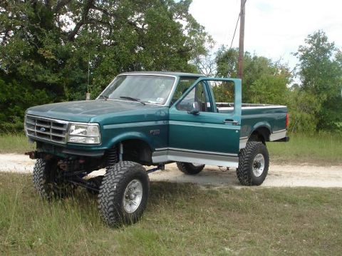 1996 Ford F-150 - This lifted 1996 Ford F-150 pickup truck is shown with its driver's door ajar, parked outdoors on a dirt path.