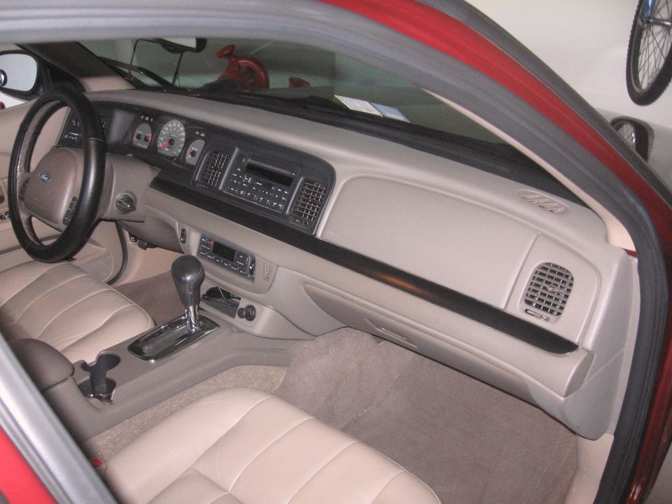 Tan leather interior and gray dash of a red Ford Crown Victoria seen through open passenger door
