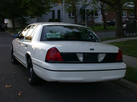 2000 Ford Crown Victoria - White 2000 Ford Crown Victoria sedan parked curbside on a street with houses in the background.