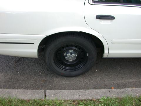 2000 Ford Crown Victoria - The rear wheel and side of a white sedan are visible.