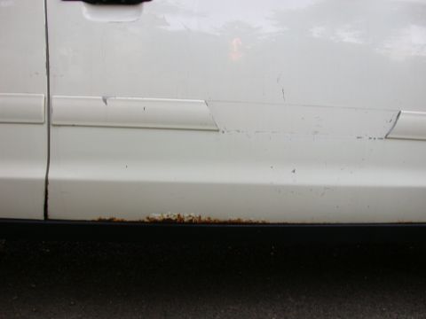 2000 Ford Crown Victoria - Close-up of a white car door showing rust damage along the lower panel and a damaged trim piece.