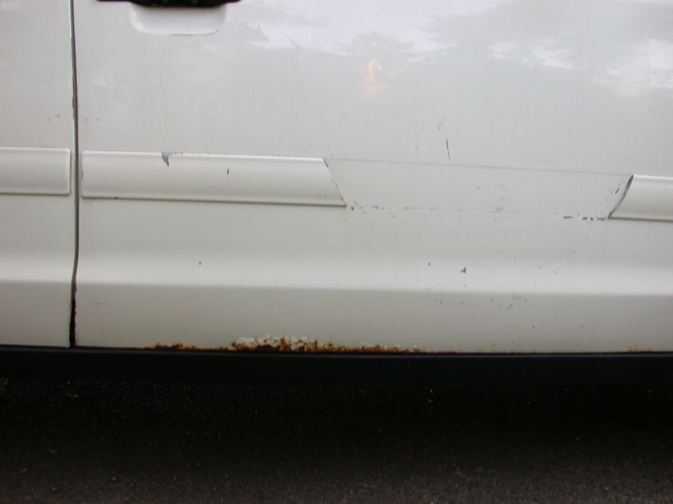 White car door with rust along the bottom edge and damage to the trim