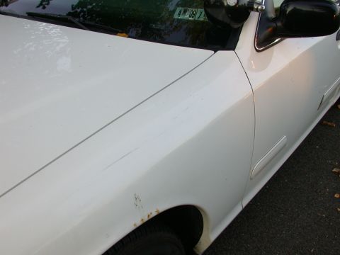 2000 Ford Crown Victoria - The front fender of a white sedan shows signs of wear, including rust and minor scratches.