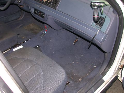 2000 Ford Crown Victoria - The interior of a 2000 Ford Crown Victoria shows the driver's seat, dashboard, and floor with visible wear and loose wiring.