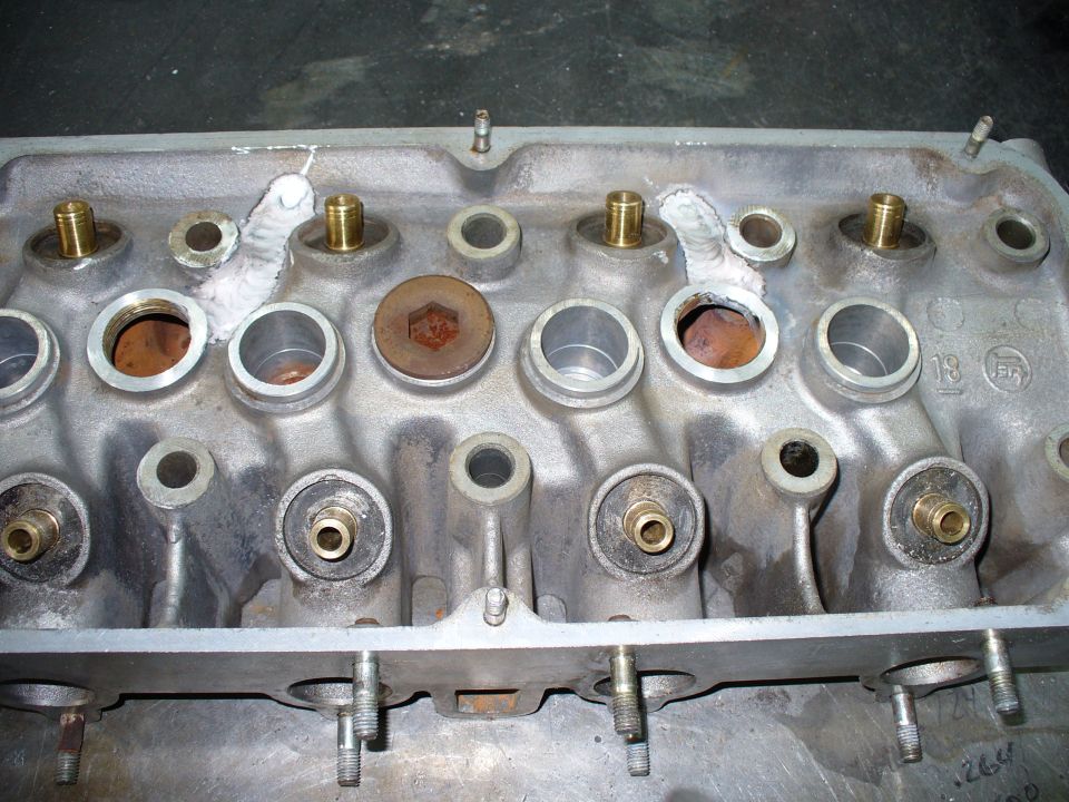 Bare four-cylinder aluminum cylinder head, deck side up, with weld repairs between chambers