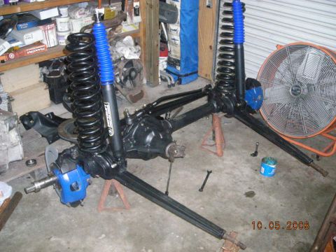 1993 Ford Bronco - Front axle assembly with black springs and blue shocks is disassembled and resting on jack stands.