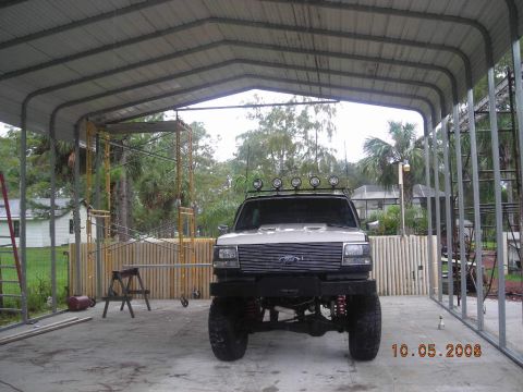 1993 Ford Bronco - This lifted Ford truck is parked under a metal carport with scaffolding nearby.