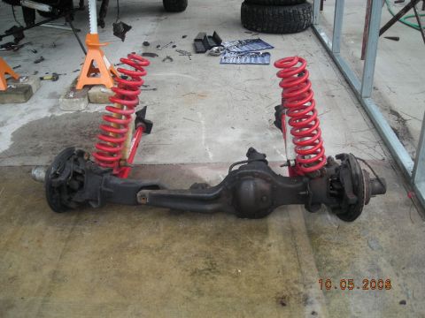 1993 Ford Bronco - A disassembled front axle assembly with bright red coil springs is shown on a concrete floor.