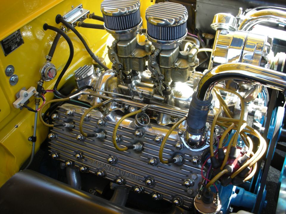 Close-up of a V8 engine with dual carburetors, chrome valve covers, and yellow spark plug wires