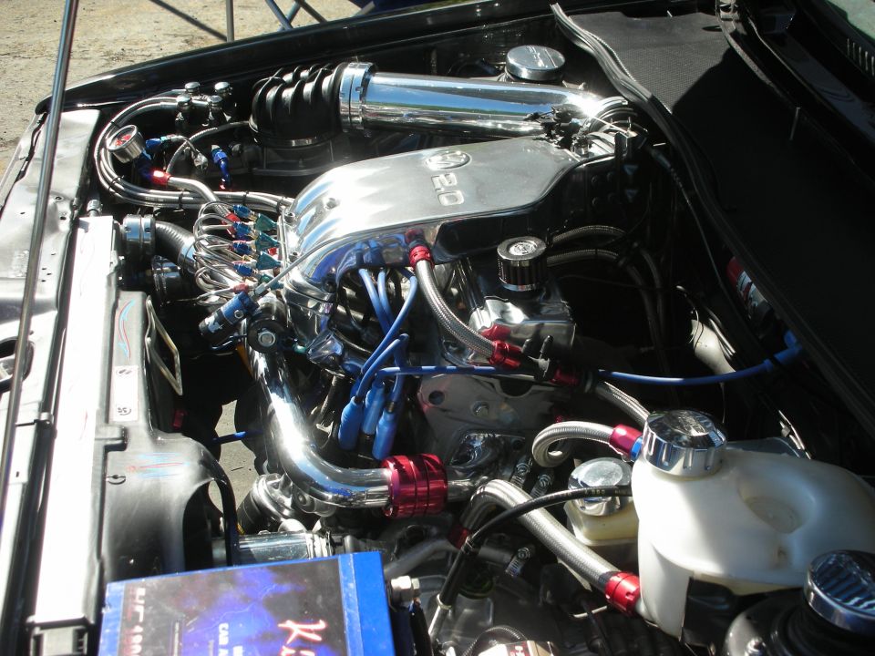 Engine bay with chrome intake manifold labeled 2.0, blue spark plug wires, and red fittings