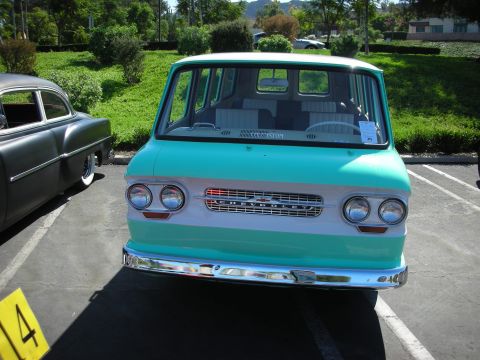 1998 Ford Crown Victoria - A teal and white Chevrolet van is parked next to a dark-colored classic car at an outdoor event.