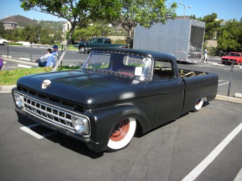 1998 Ford Crown Victoria - A modified 1957 Ford F-100 pickup truck is parked in a lot next to other vehicles and a large trailer.