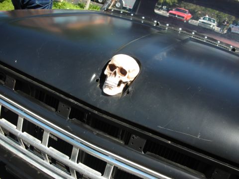 1998 Ford Crown Victoria - A skull serves as a unique hood ornament on this black vehicle, seen at a car show with other vehicles in the background.