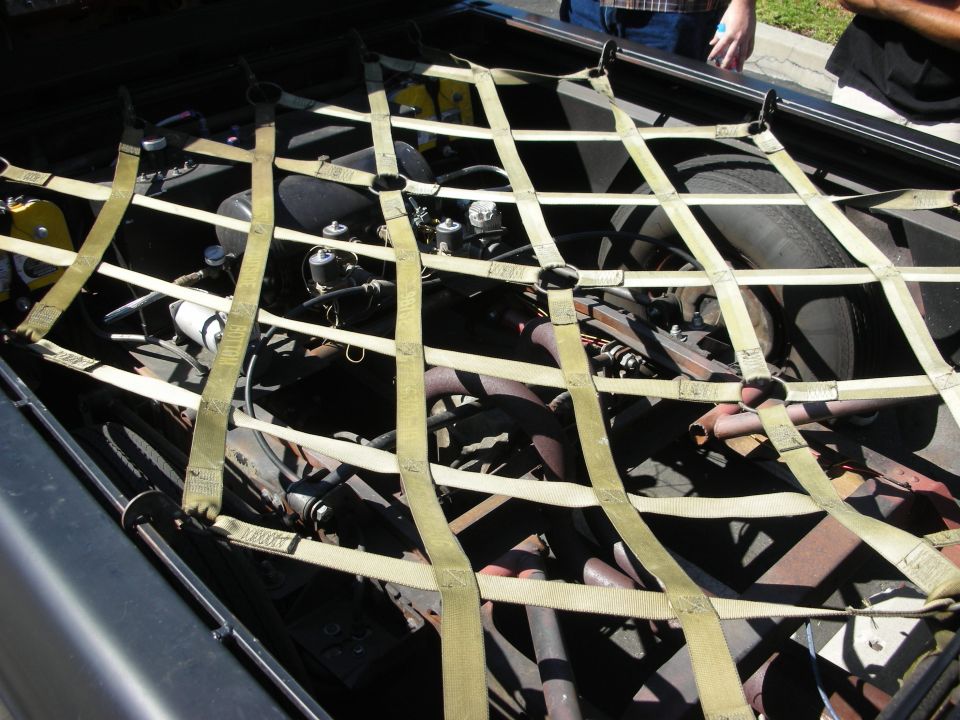 Engine bay covered by a cargo net, showing engine parts and a spare tire