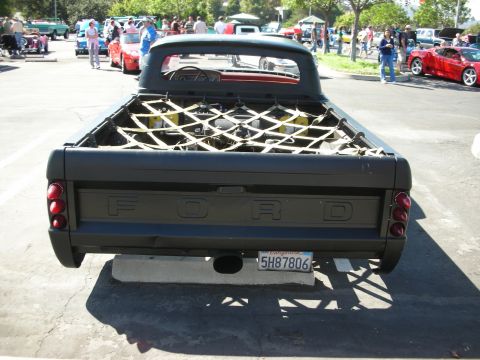 1998 Ford Crown Victoria - Rear view of a black pickup truck with a cargo net covering the engine in the bed, seen at a car show.