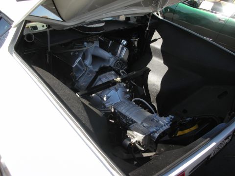 1998 Ford Crown Victoria - The engine compartment of a white car is open, revealing the supercharger and transmission, with another car visible in the background.